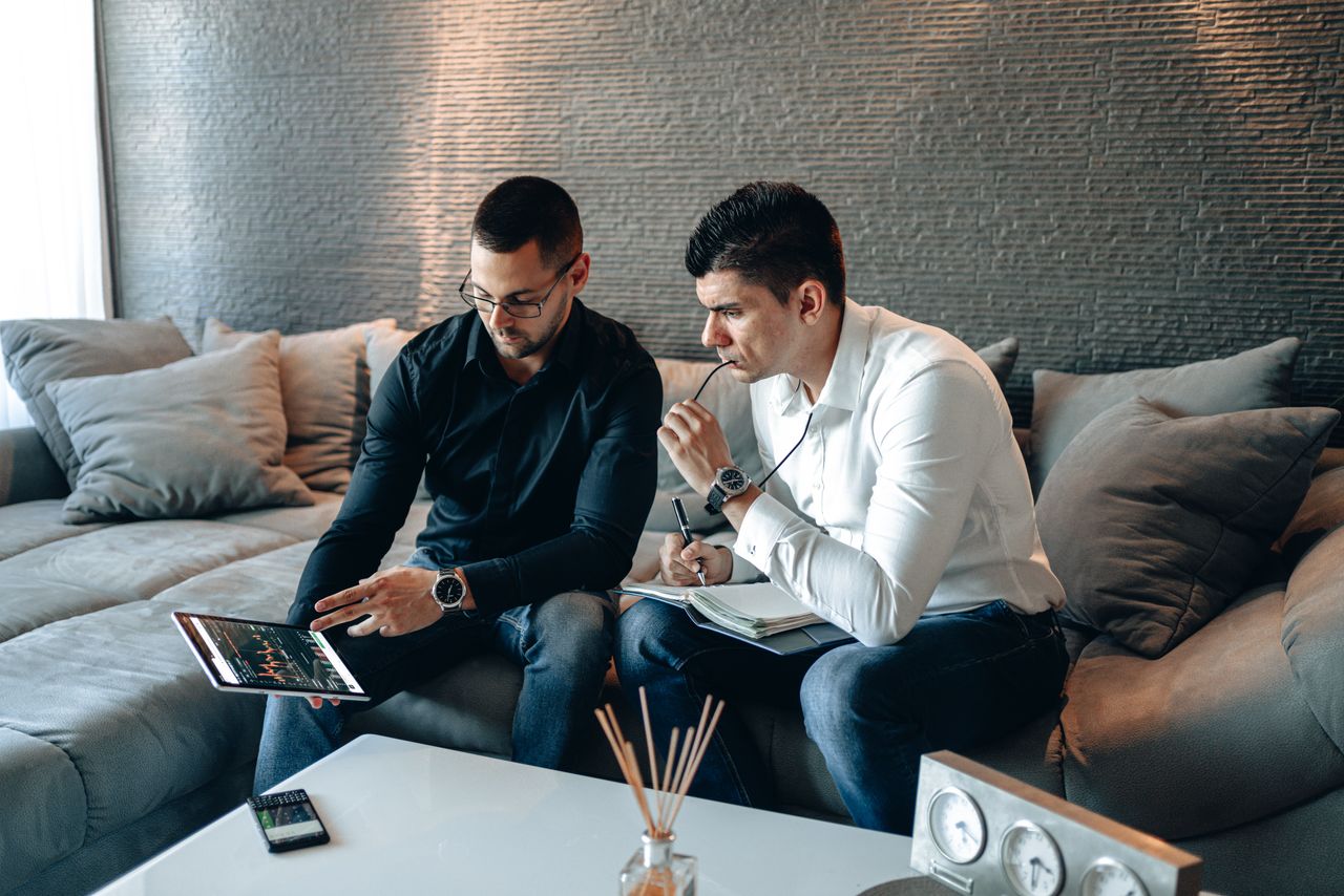 About Two business professionals on a sofa analyzing financial graphs on a digital tablet indoors.